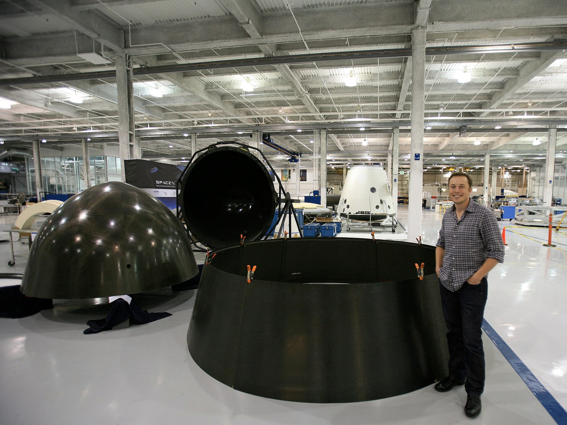 Elon Musk standing beside Dragon capsule structures inside a SpaceX factory
