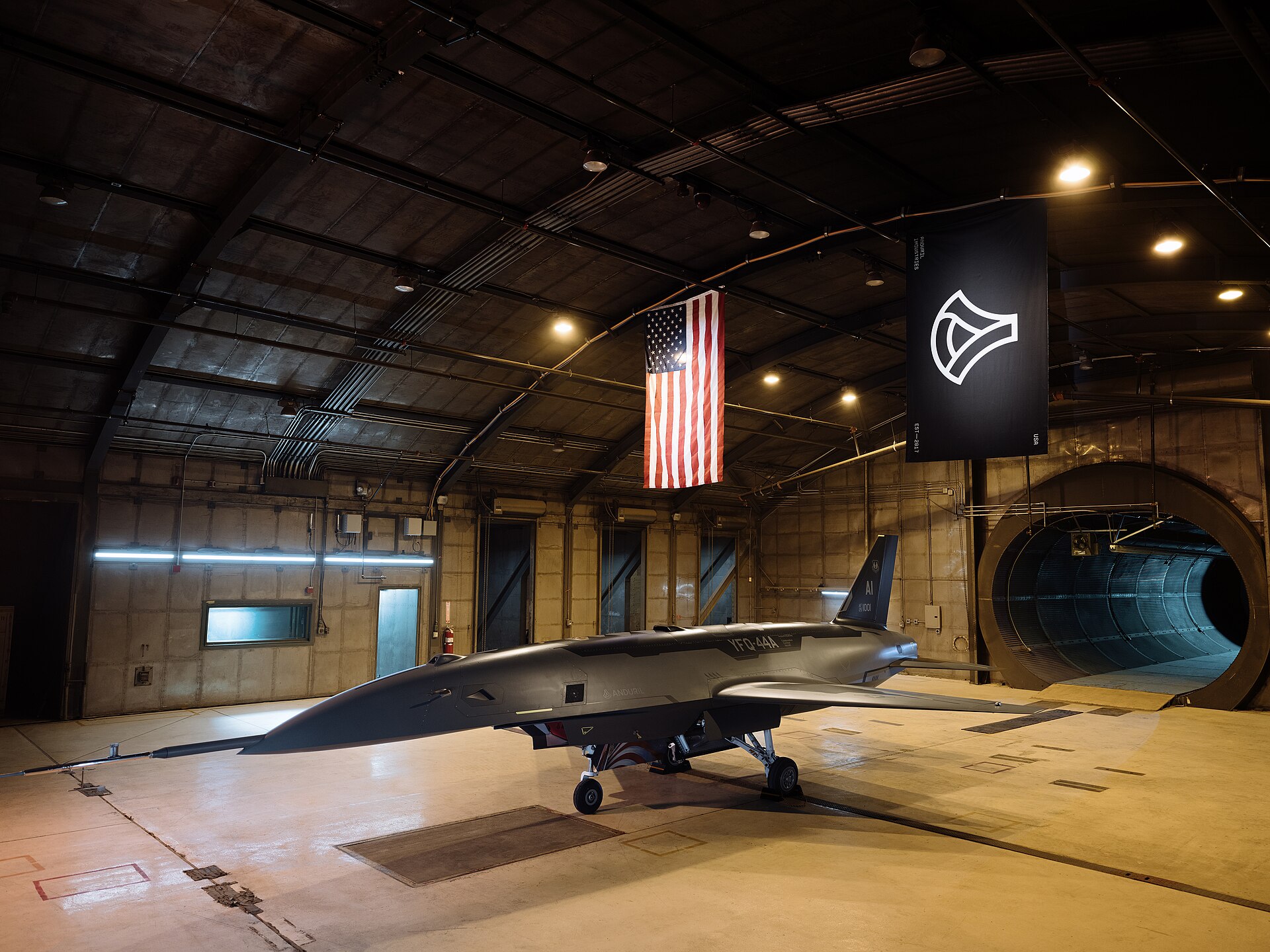 Anduril's YFQ-44A Fury combat drone in a hangar beneath a US flag and an Anduril banner during Air Force ground testing