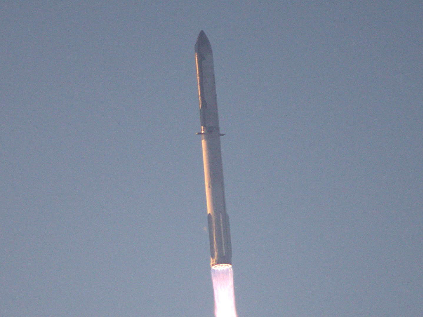 The Starship full stack climbing under powered ascent against a clear sky, shortly after liftoff.