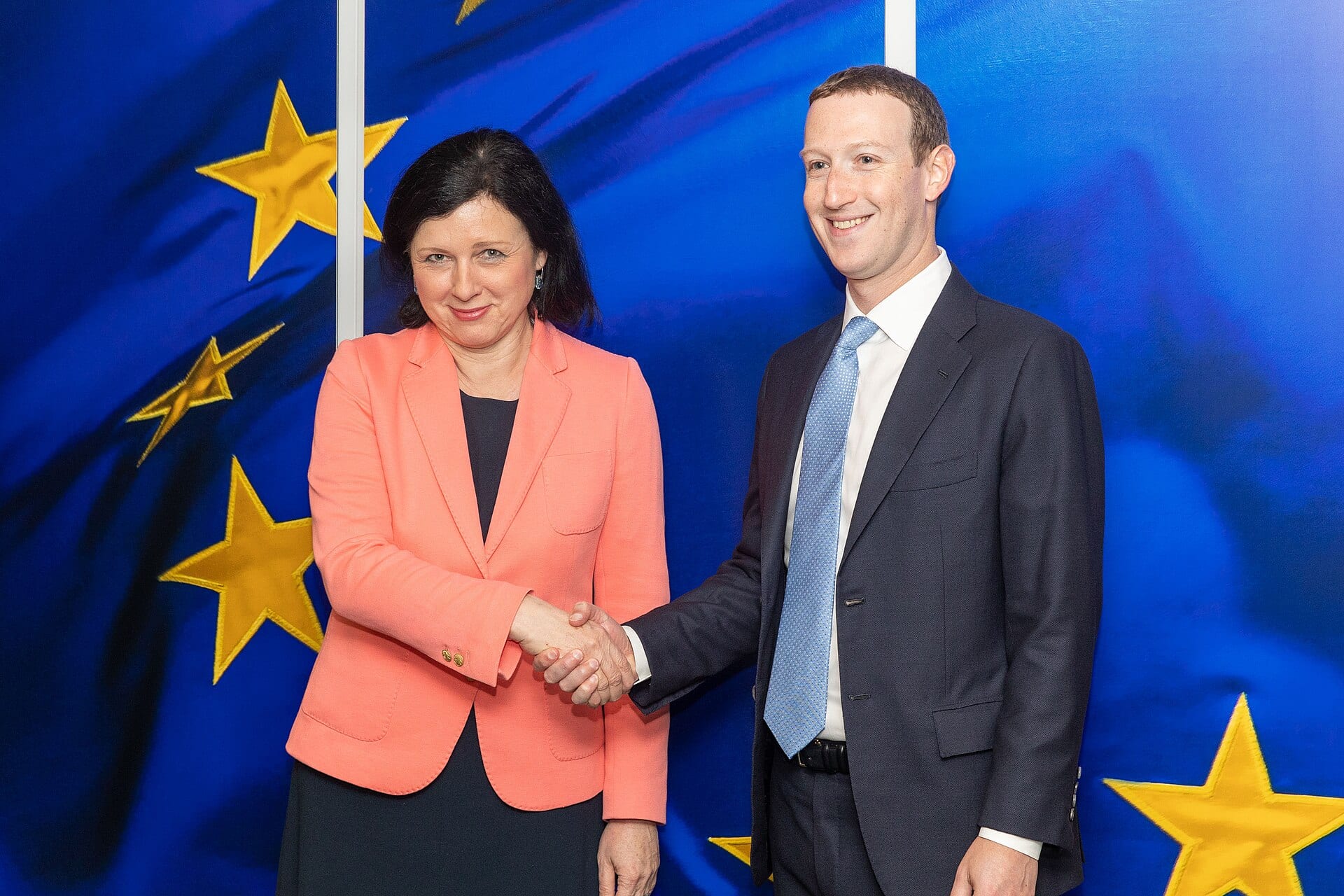 Mark Zuckerberg shakes hands with European Commission Vice-President Vera Jourova in front of EU flags