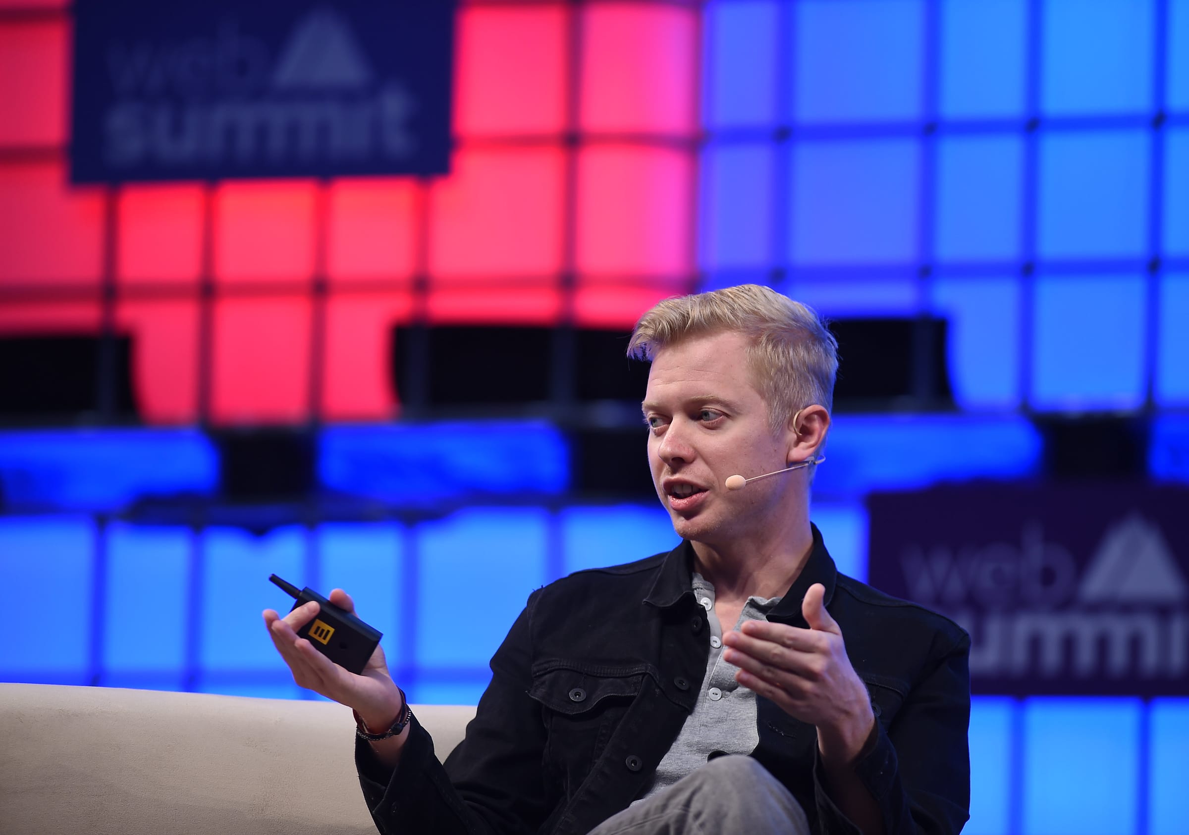 Reddit CEO Steve Huffman speaking on stage at Web Summit 2017, gesturing with a clicker in hand against a wall of illuminated red and blue panels.