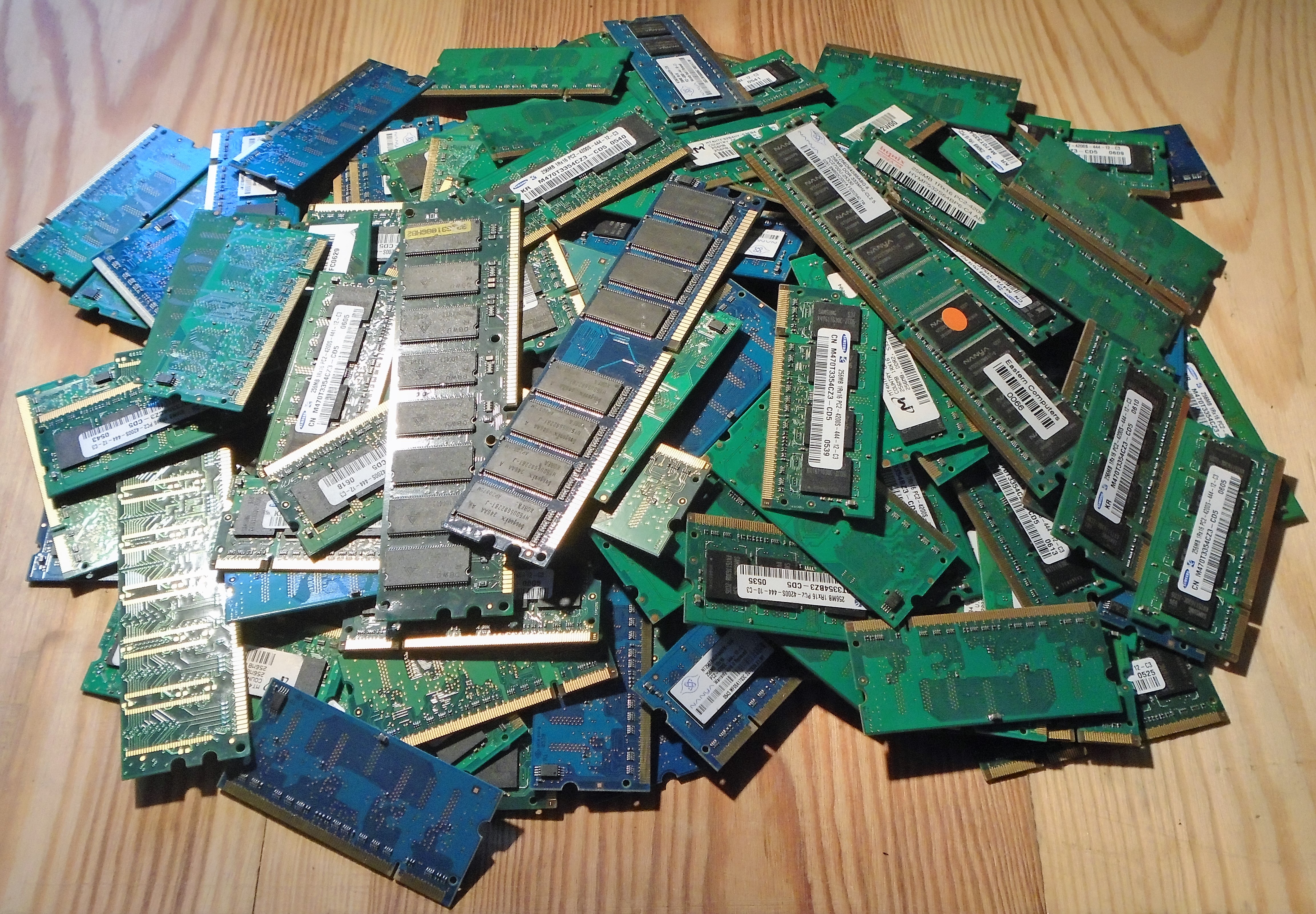 A pile of green and blue laptop and desktop RAM memory modules on a wooden surface