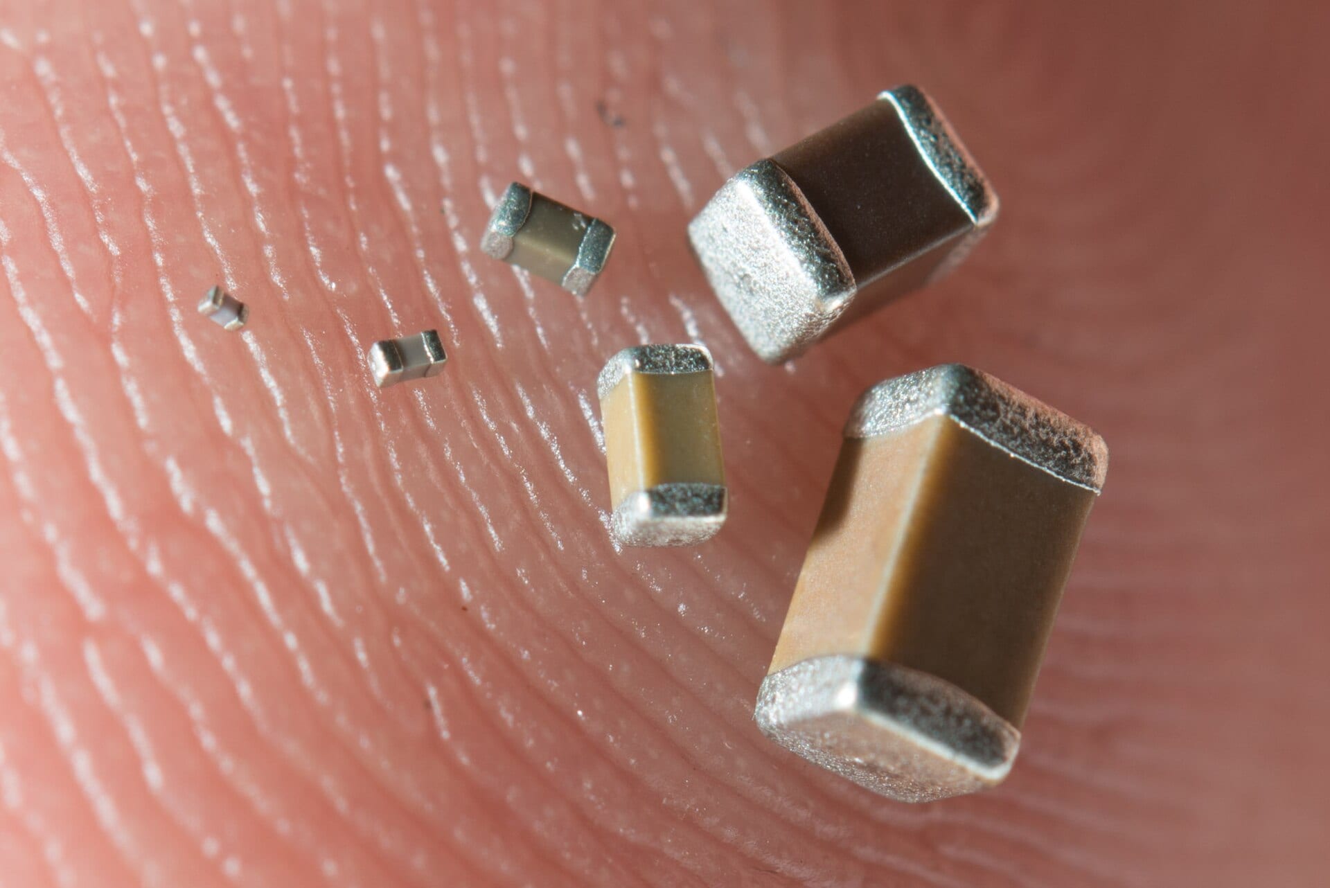 Six multilayer ceramic capacitors of increasing size resting on a fingertip