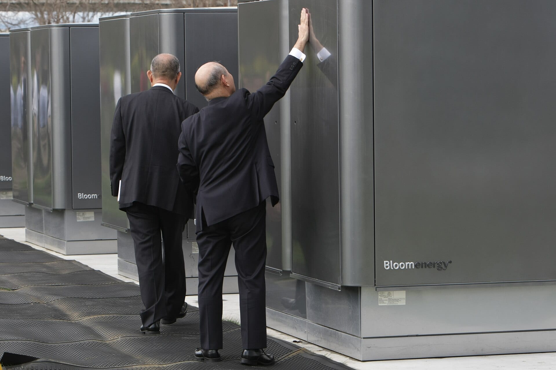 A man in a suit rests his hand on a row of dark metal Bloom Energy fuel-cell servers