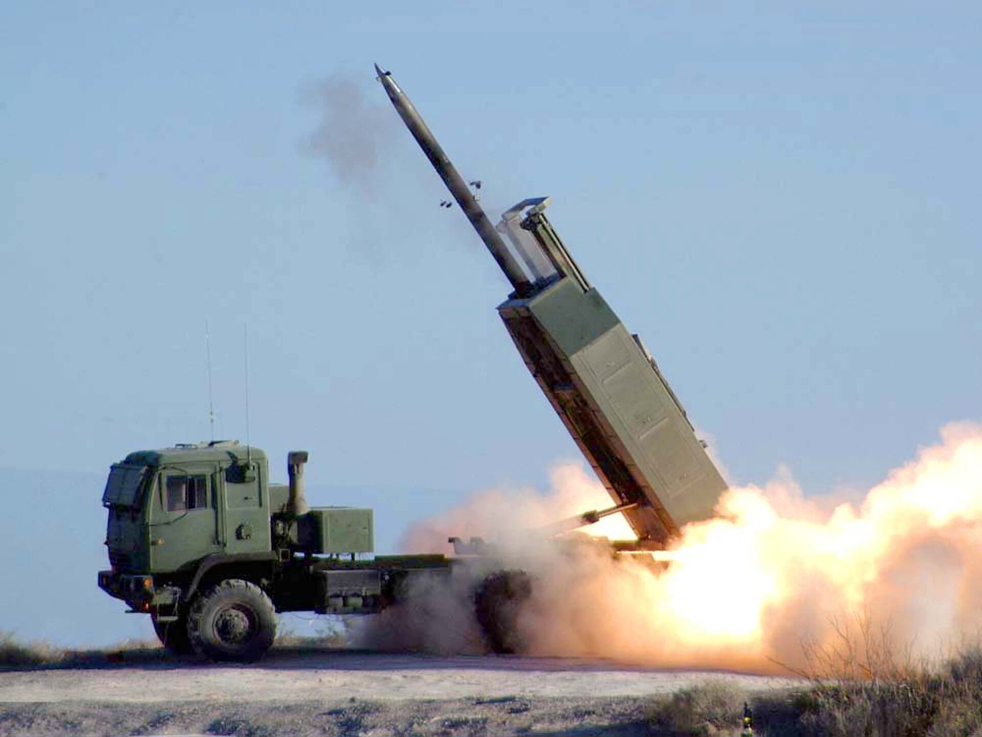A HIMARS launcher fires a guided rocket from a desert range, smoke billowing as the missile climbs