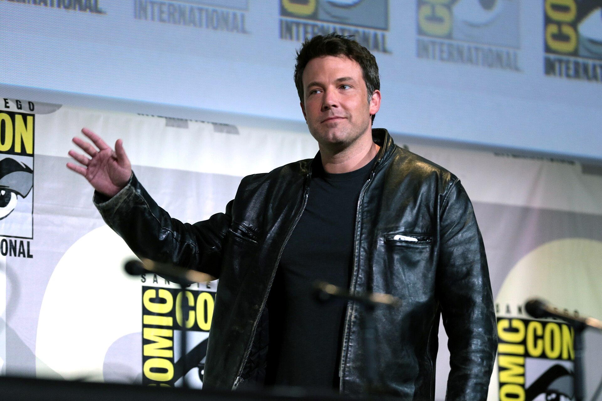 Ben Affleck gesturing on stage at a Comic-Con panel