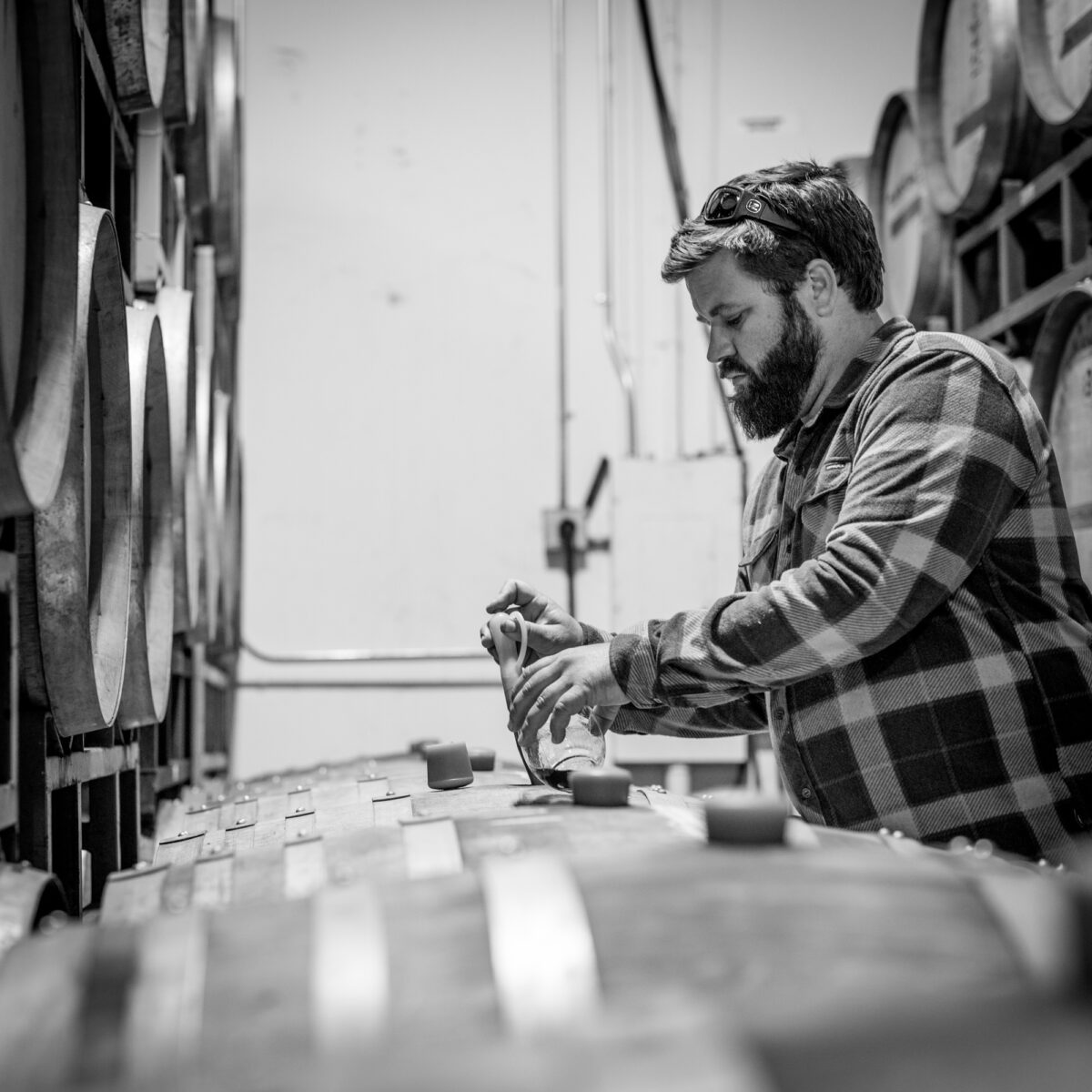 Drake Whitcraft, of Whitcraft Winery, standing over wine barrels. The photo is black and white.