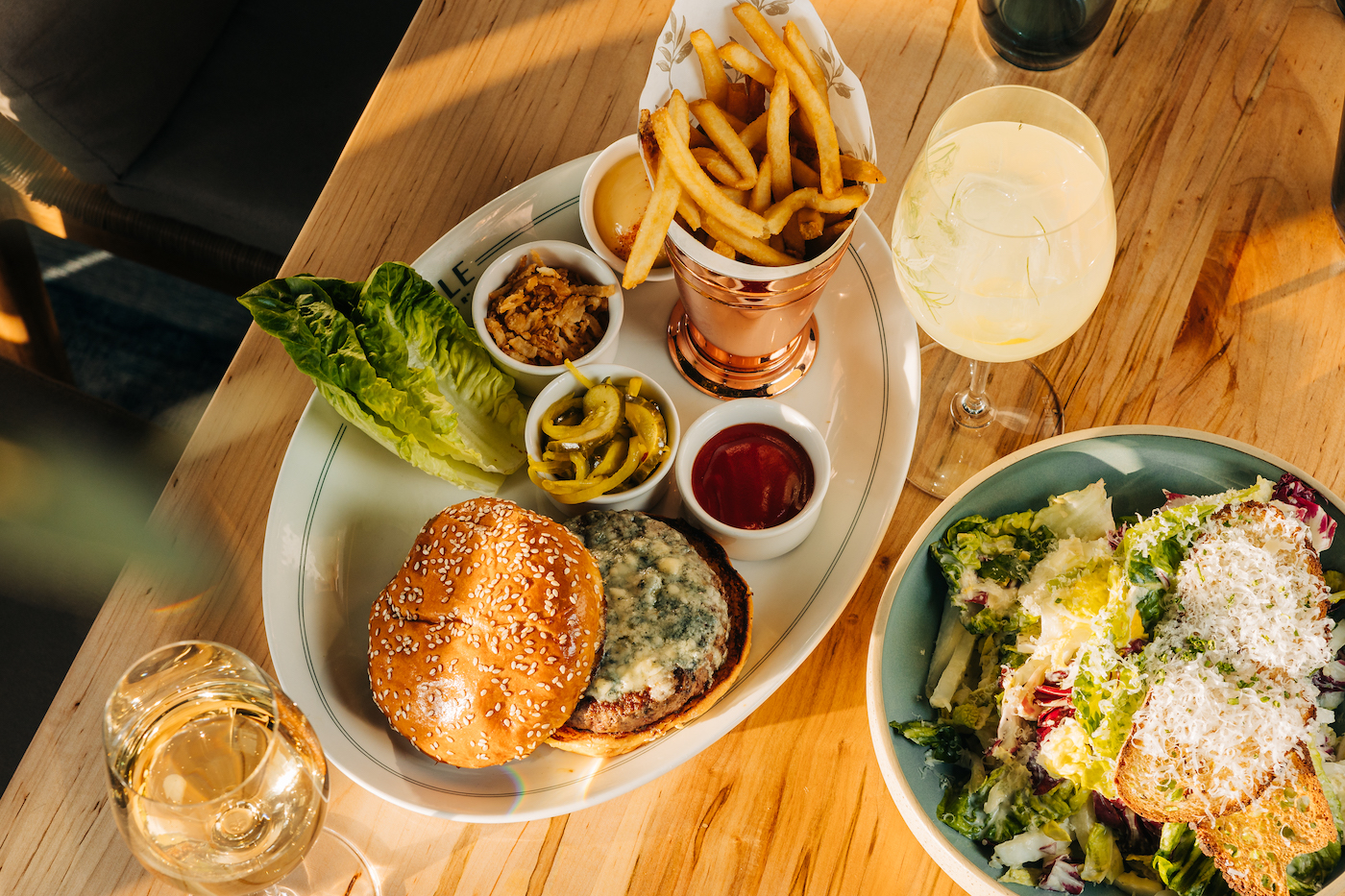 The Oakville's dry-aged steak burger with blue cheese, garnishments, and french fries, the Napa Caesar salad, and beverages.