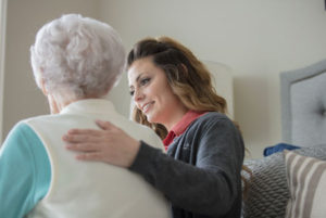 A health care professional places her arm around an elderly woman in a comforting gesture