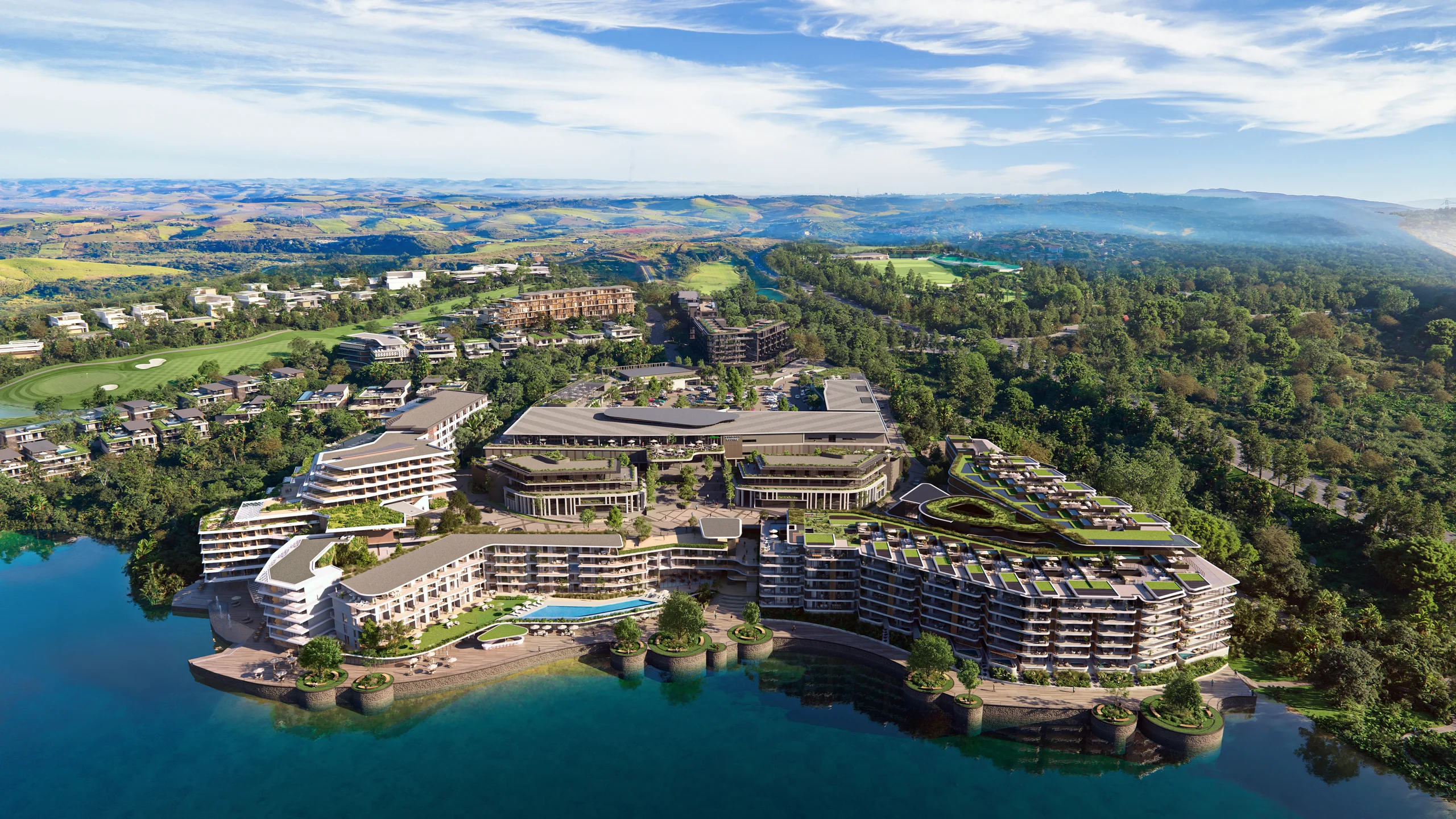 Aerial across the lake of the Tatali Precinct at Zimbali, Vilasita's residences at the water's edge, forest and rolling hills beyond, under a clear sky