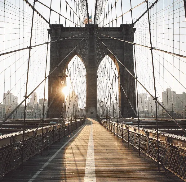 Pasarela peatonal del Puente de Brooklyn con el sol entre sus estructuras.
