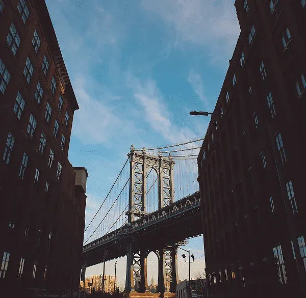 Vista del Puente de Manhattan entre edificios de Brooklyn al atardecer.