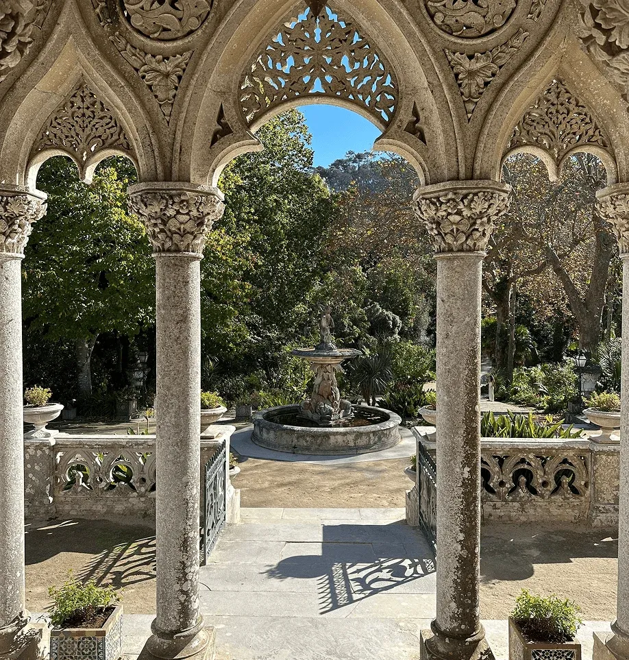 Galleria porticata del Palazzo di Quinta da Regaleira con vista su una fontana e i giardini storici di Sintra.