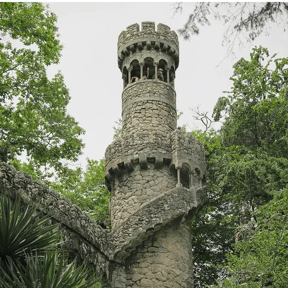 Steinturm von Quinta da Regaleira umgeben von Gärten in Sintra, mit Außentreppe.