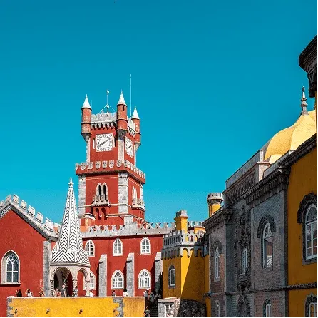 Red clock tower and colorful architecture of Pena Palace in Sintra under a clear blue sky.