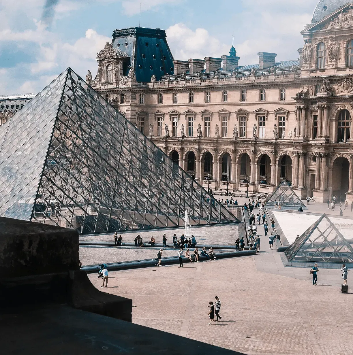 Visitors walking through the Louvre Museum courtyard surrounded by historic palace buildings and the glass pyramid.