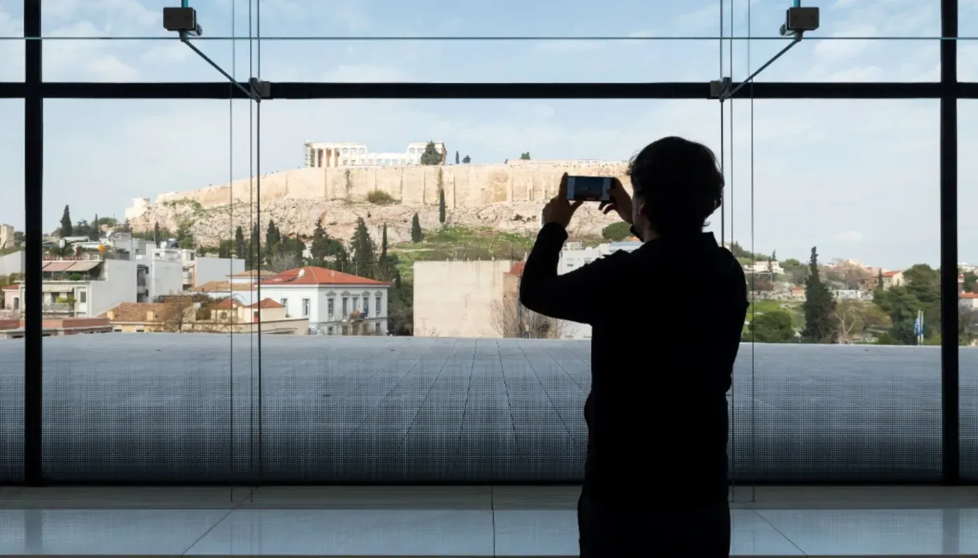 Visitor photographing the Acropolis from inside the Acropolis Museum in Athens.
