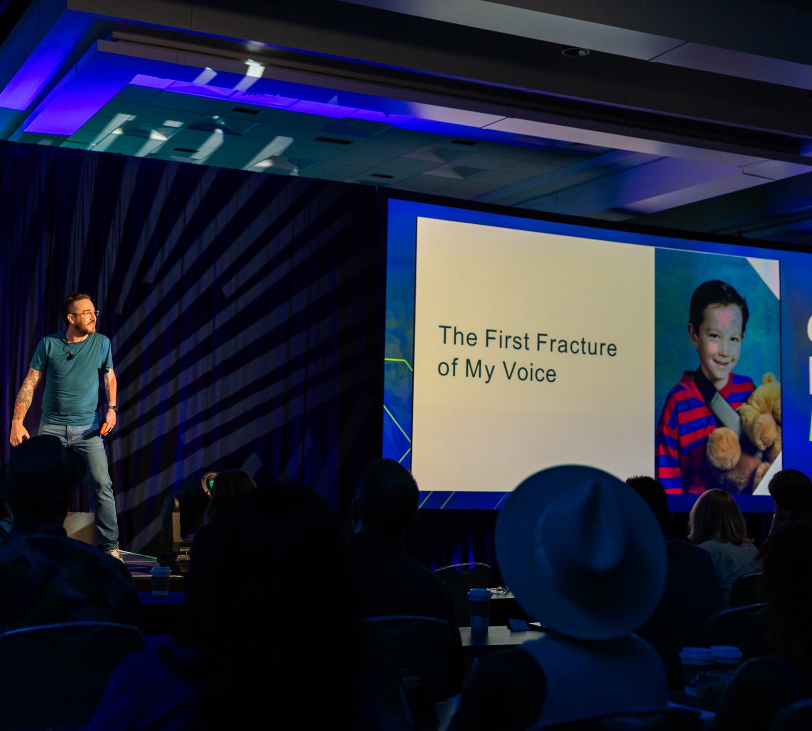 Brian Bogert on stage telling his story with 'The First Fracture of My Voice' slide and childhood photo