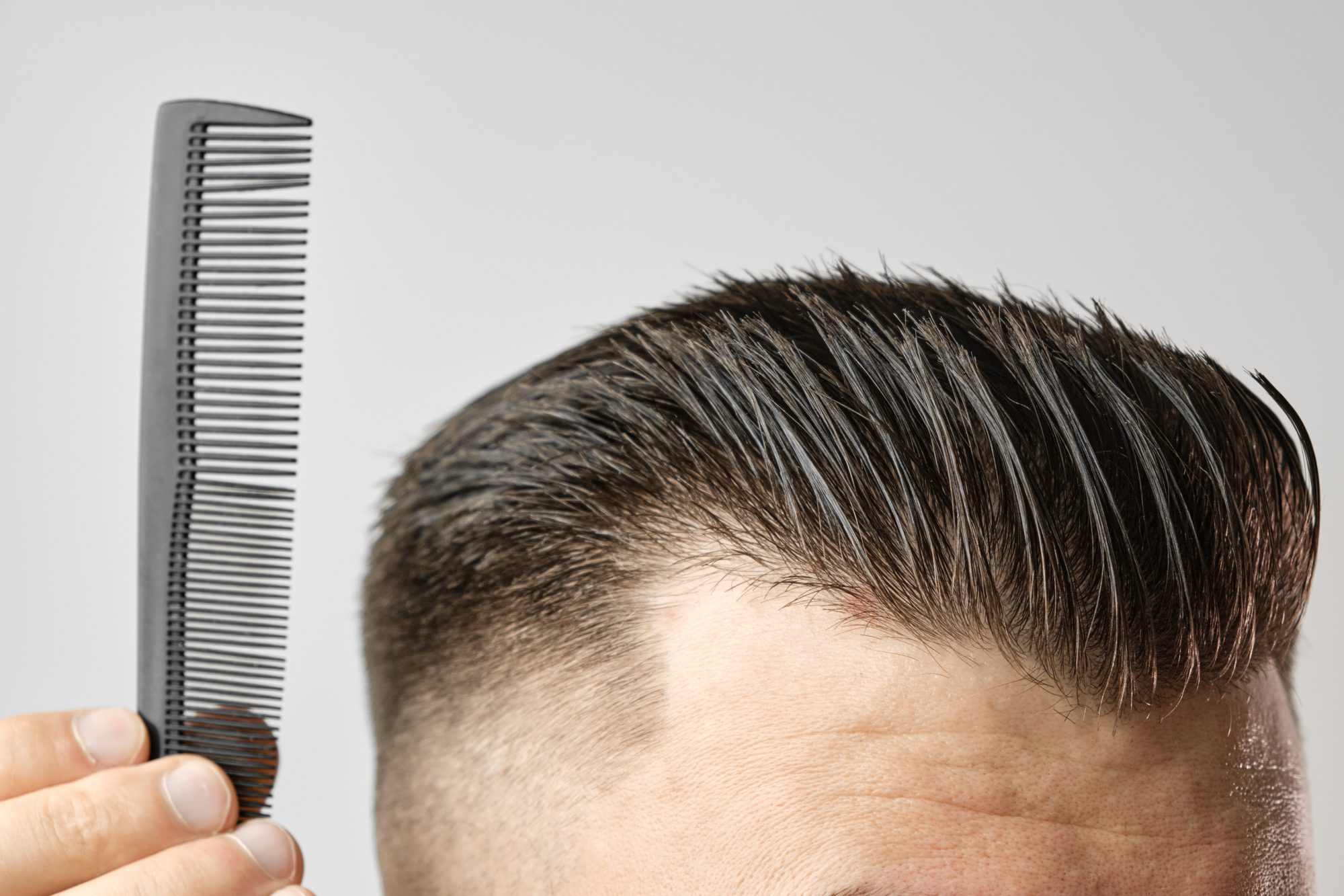 Close up young man combing his hair with a plastic comb. Styling hair after barbershop