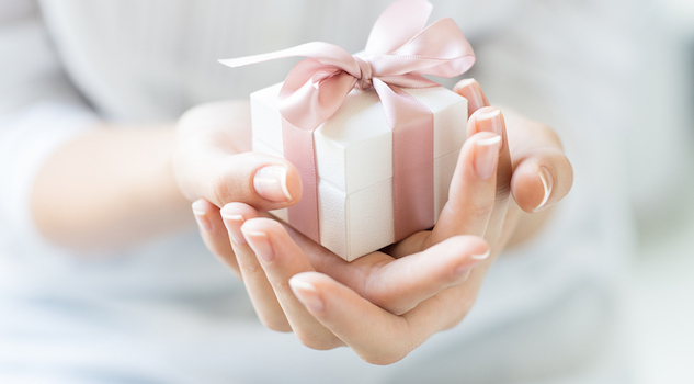 Close up shot of female hands holding a small gift wrapped with pink ribbon. Small gift in the hands