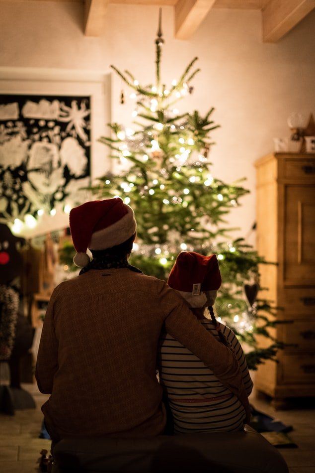 a parent sits by a Christmas tree with their children