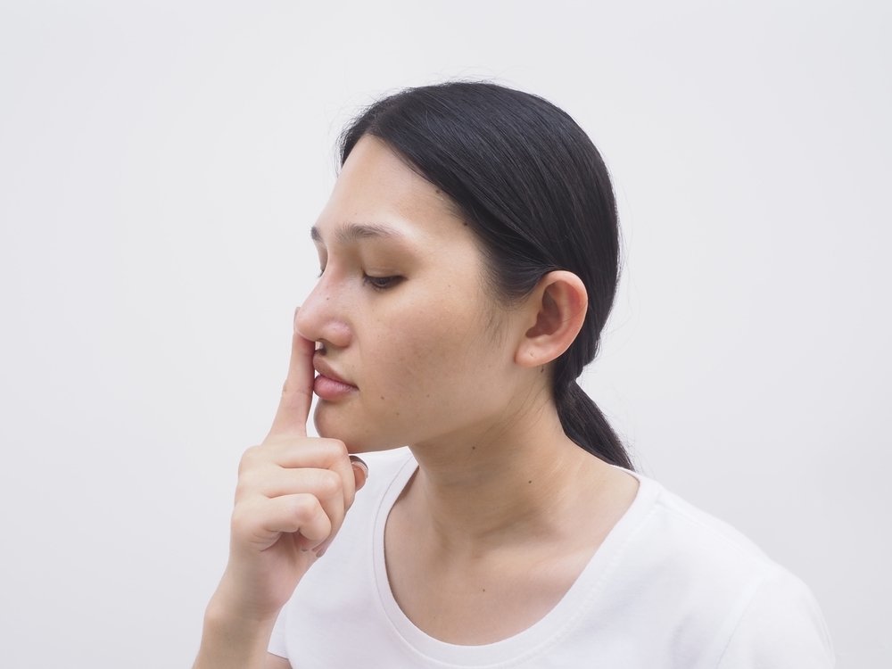A woman touching her nose, possibly experiencing nasal discomfort, airway blockage, or sinus infection. This image represents breathing difficulty, respiratory discomfort, and throat irritation, makin