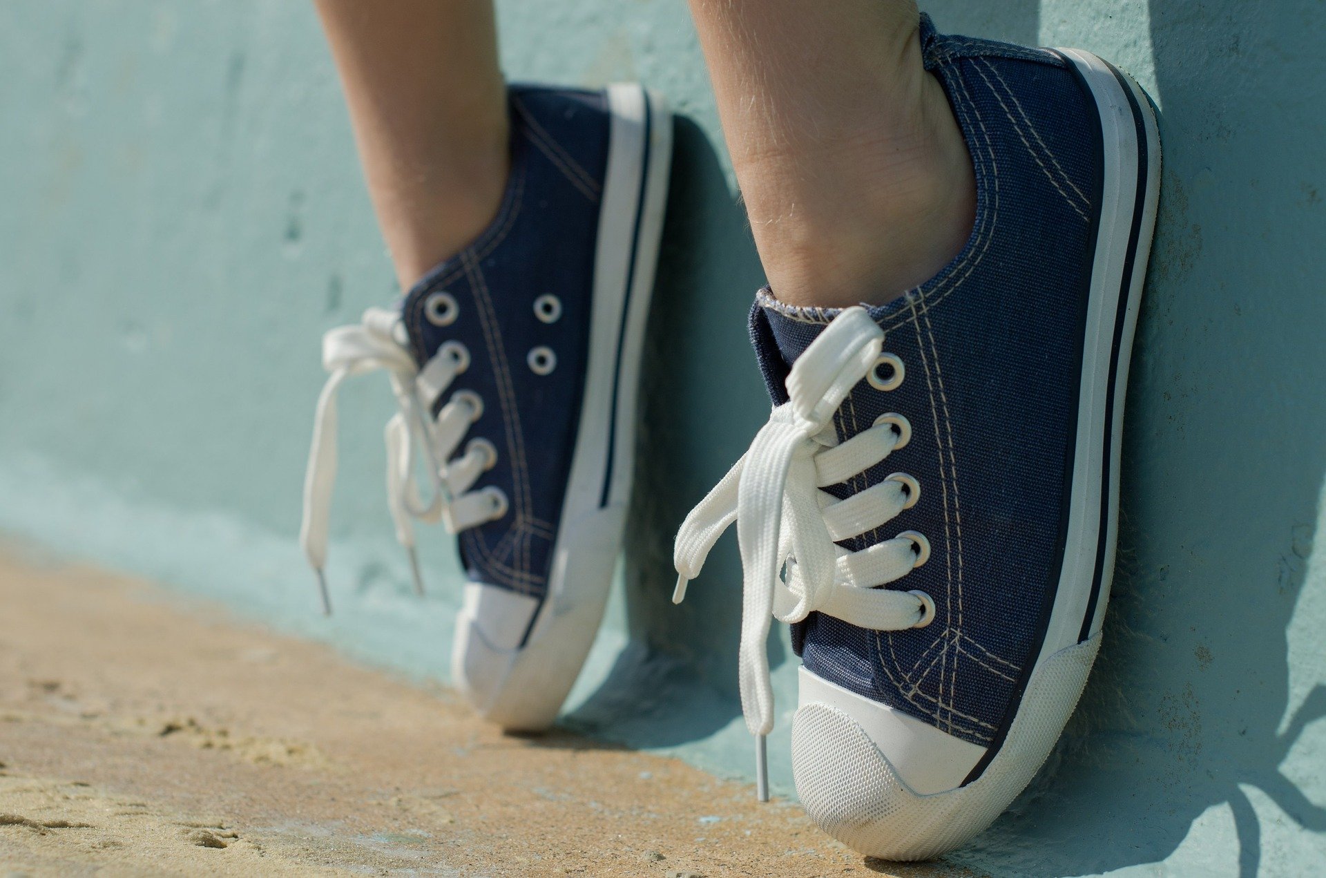 person wearing sneakers rests their feet on blue wall