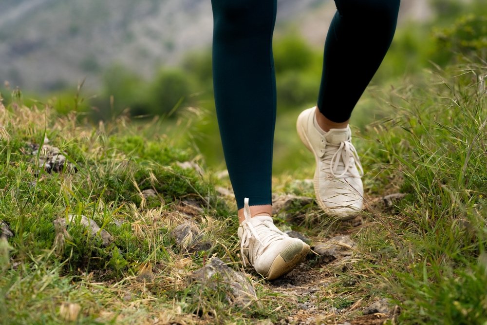 Woman spraining ankle while running outdoors, wear outfit leggings and white sneakers, close-up of foot twisting on uneven grass surface, risk of sports injury and leg trauma during outdoor activity