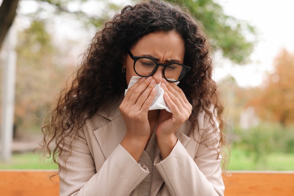 A woman sneezing into a tissue outdoors during fall ragweed allergy season