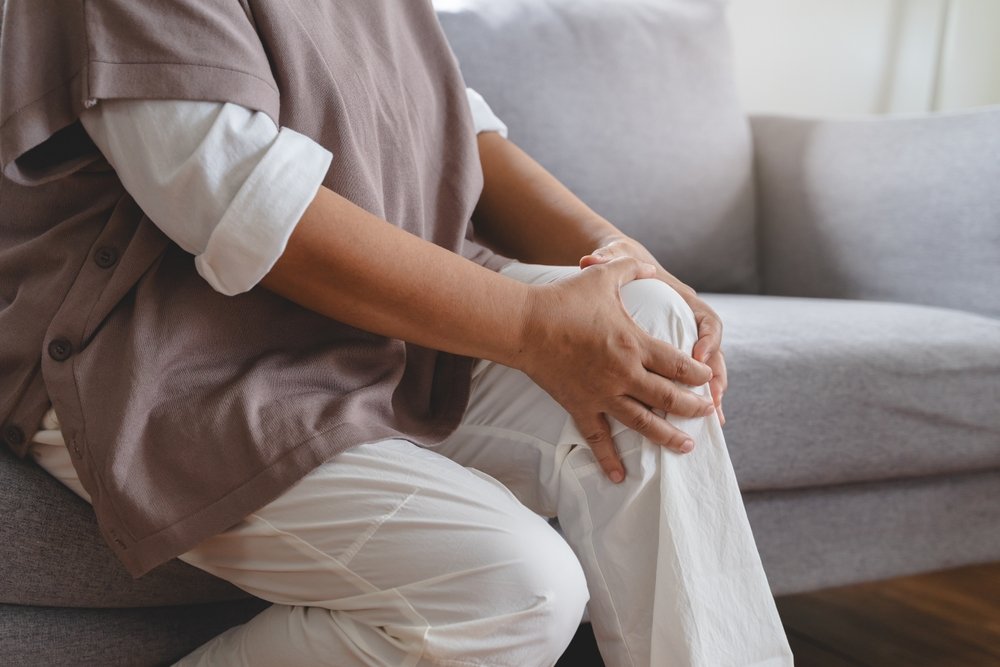 Person holding their knee in pain while seated on a couch at OAA Orthopaedic Specialists, PA