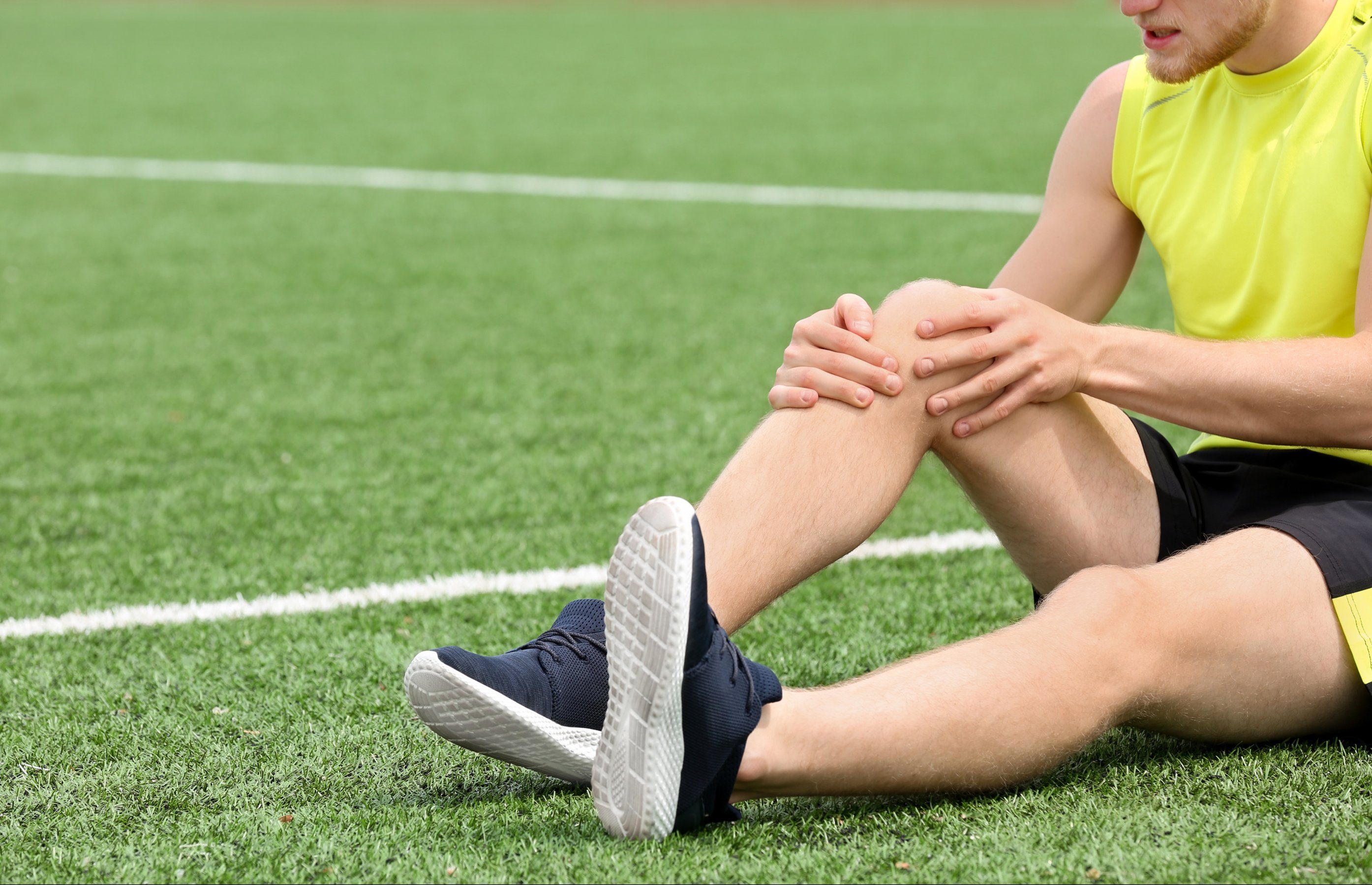 Man in sportswear suffering from knee pain at soccer field