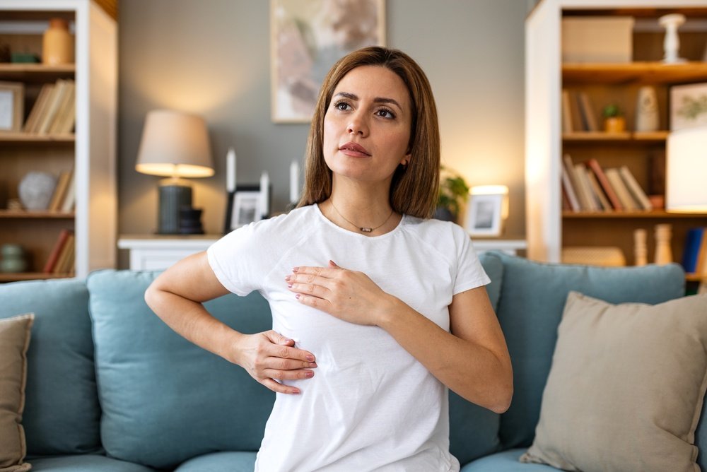 Breast self examination. Health check at home, Woman with chest problem, Healthcare and medicine concept. Attractive female sitting on sofa and touching chest to check for lumps and cancer signs.