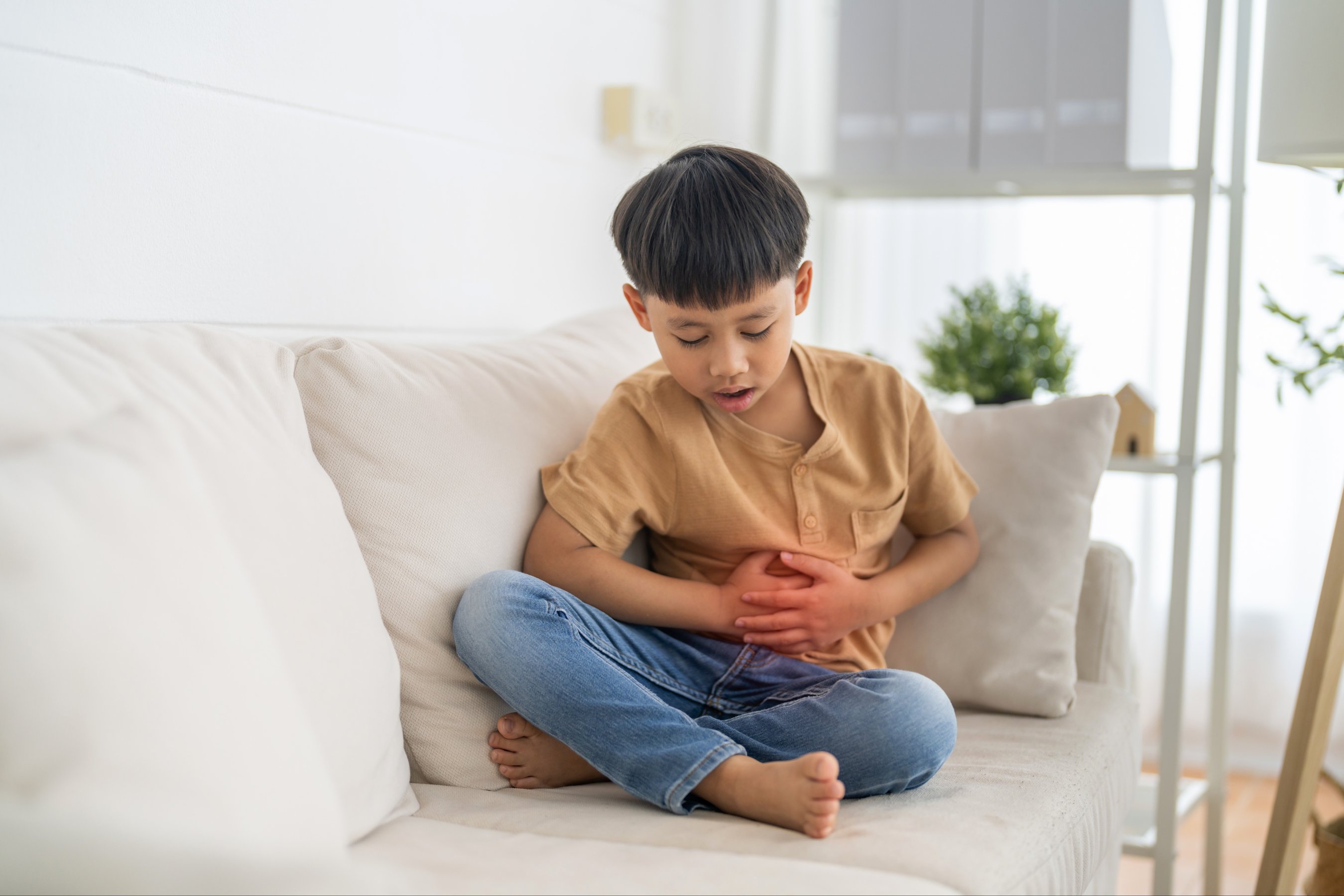 sick unhappy little child asian boy touching belly stomach