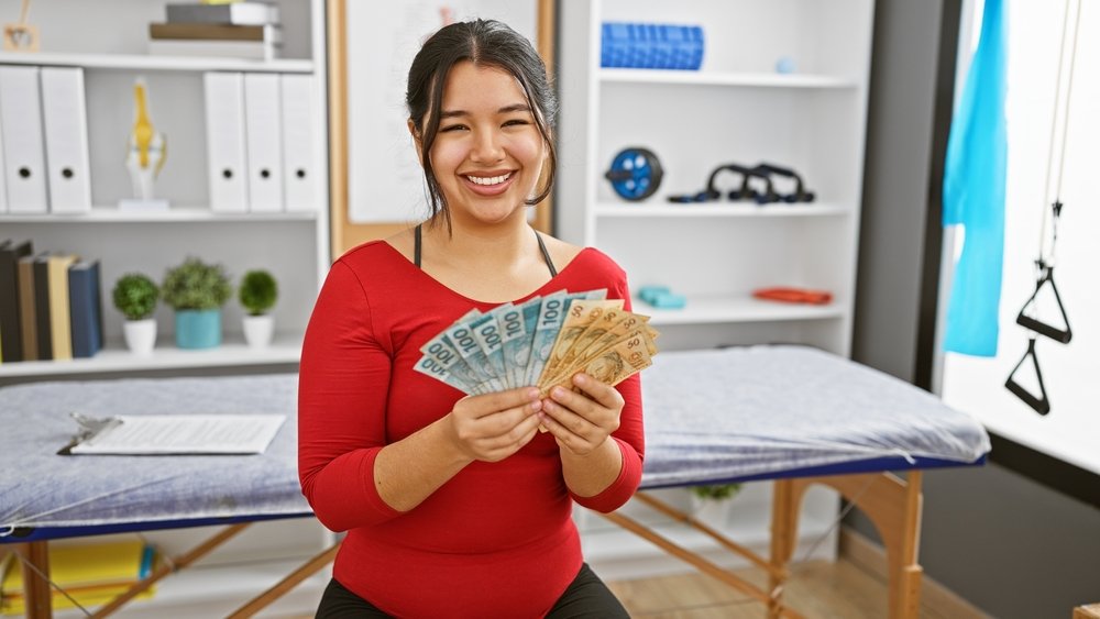 A smiling woman holds brazilian reais in a physiotherapy clinic