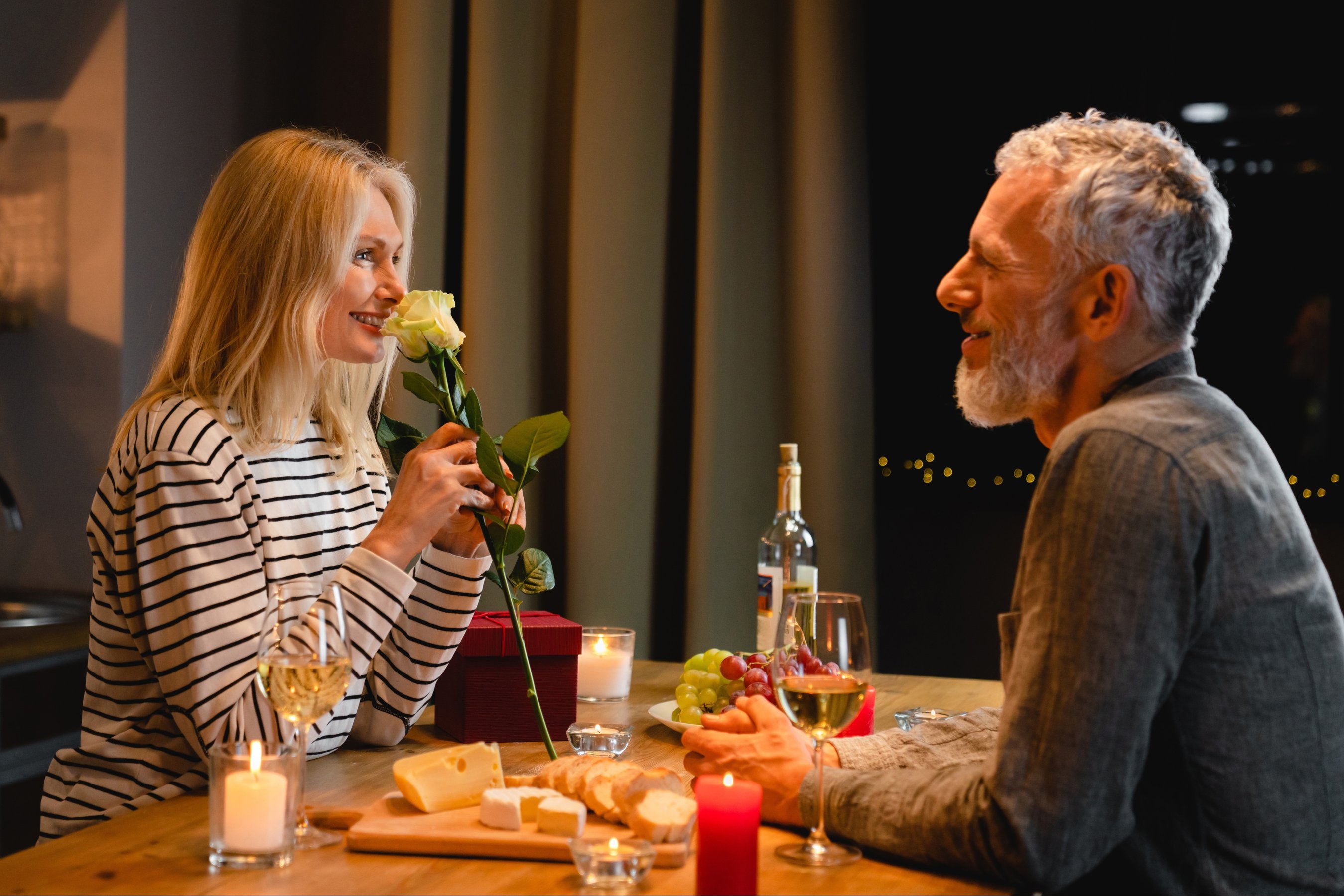 Happy middle-aged woman enjoying the rose fragrance during romantic dinner