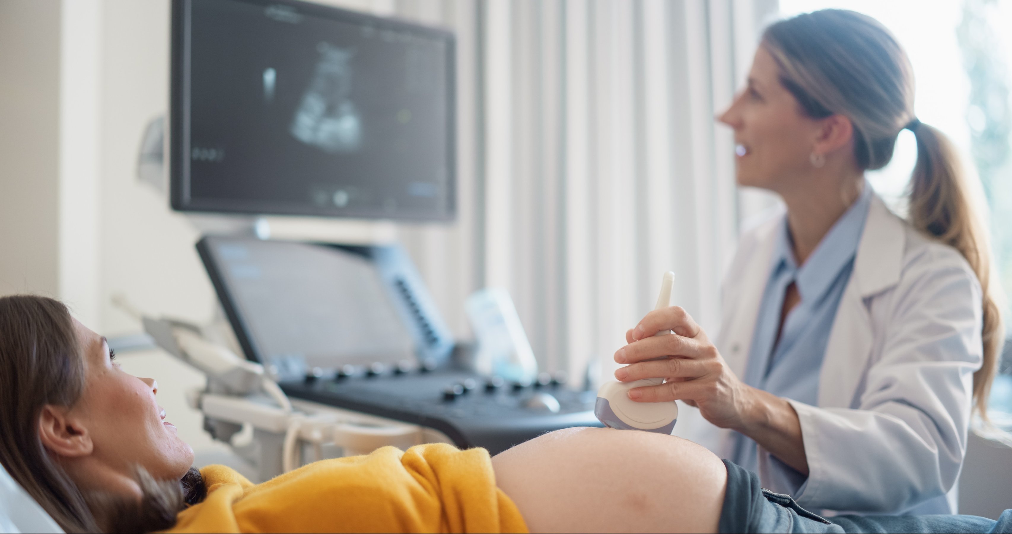 Young Pregnant Woman Lies on a Clinic Bed while a Female Obstetrician Performs an Ultrasound Procedure