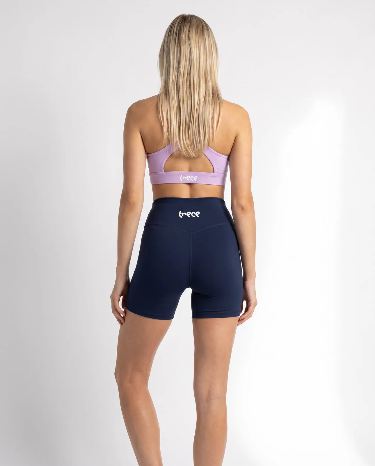 Mujer descalza de espaldas con top lila y shorts Foundation azul marino de TRECE
