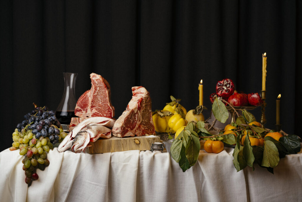 A Feast fit for a King. A table of large steaks, vegetables, fruits and candle sticks.