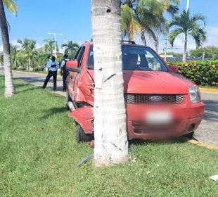 Automóvil rojo impactado contra palmera