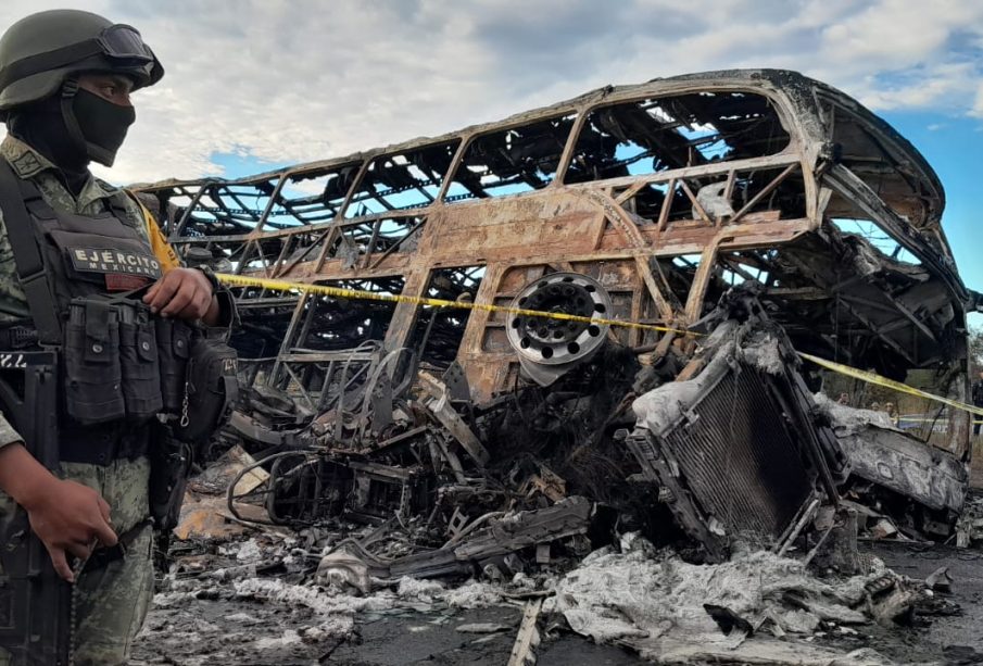 Soldado resguardando restos de autobus y tráiler incinerado