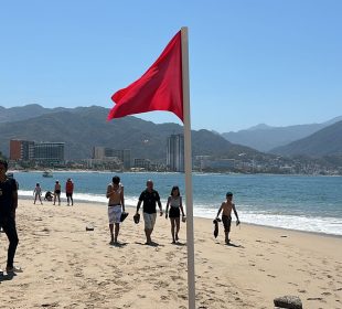 Vacacionistas paseando en playa con bandera roja