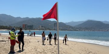 Vacacionistas paseando en playa con bandera roja