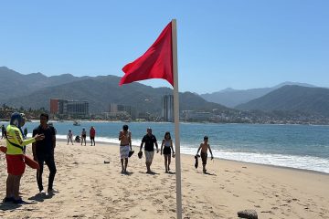 Vacacionistas paseando en playa con bandera roja