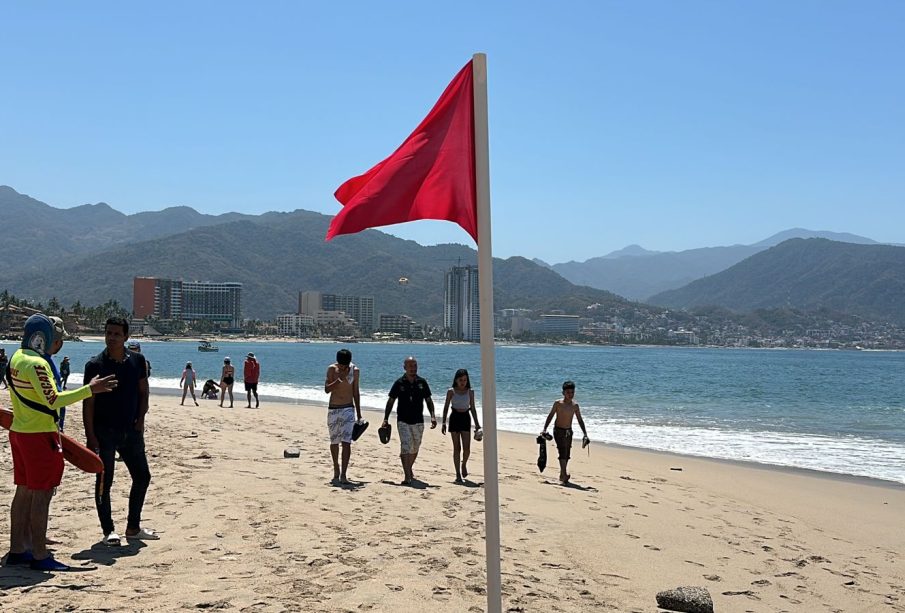 Vacacionistas paseando en playa con bandera roja