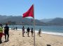 Vacacionistas paseando en playa con bandera roja