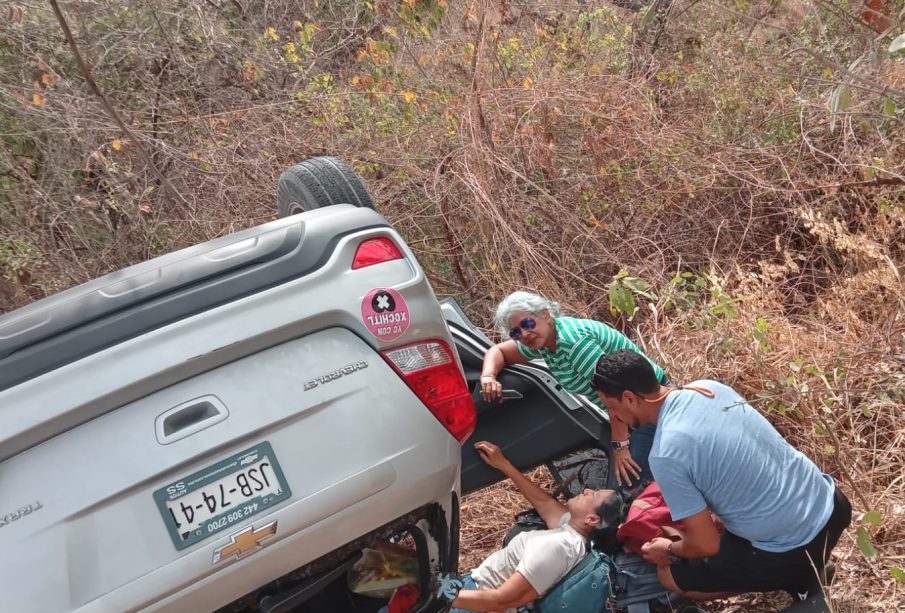 Personas dando primeros auxilios a mujer lesionada por volcadura