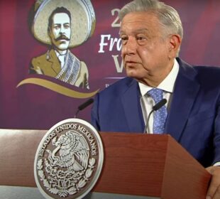 AMLO parado sujetandose del podium