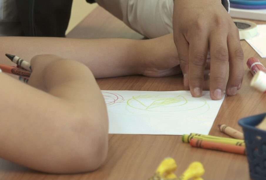 Docente dibujando junto a niño autista.