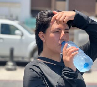 mujer tomando agua y cubriéndose del sol