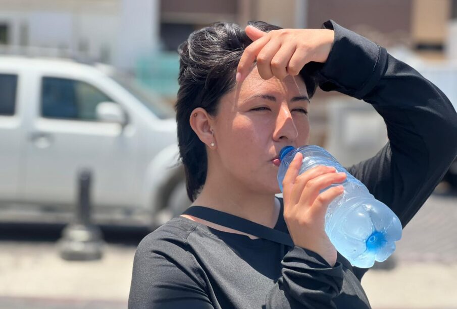 mujer tomando agua y cubriéndose del sol